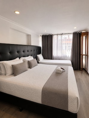 Une chambre d’hôtel avec deux lits, une tête de lit sombre et une fenêtre avec des rideaux.