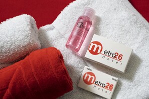 A white towel, a red towel, and two boxes of Metro26 Hotel soap and shampoo on a white towel. - Hotel Metro 26 (Bogotá)