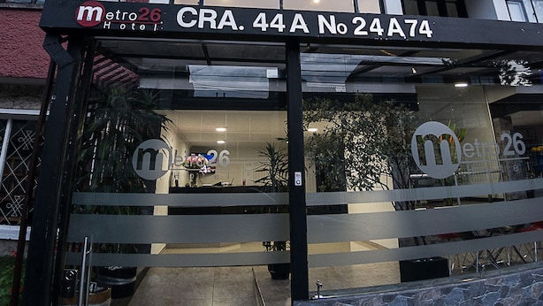 A hotel entrance with a ramp leading up to the door, a sign above the door, and a reflection of the hotel logo on the glass. - Hotel Metro 26 (Bogotá)