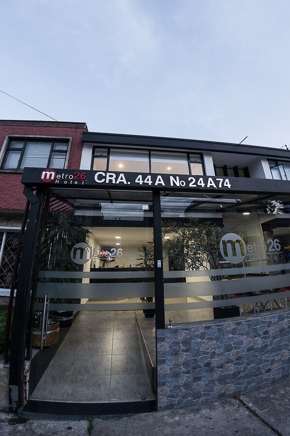 A hotel entrance with a ramp leading up to the door, a sign above the door, and a reflection of the hotel logo on the glass. - Hotel Metro 26 (Bogotá)