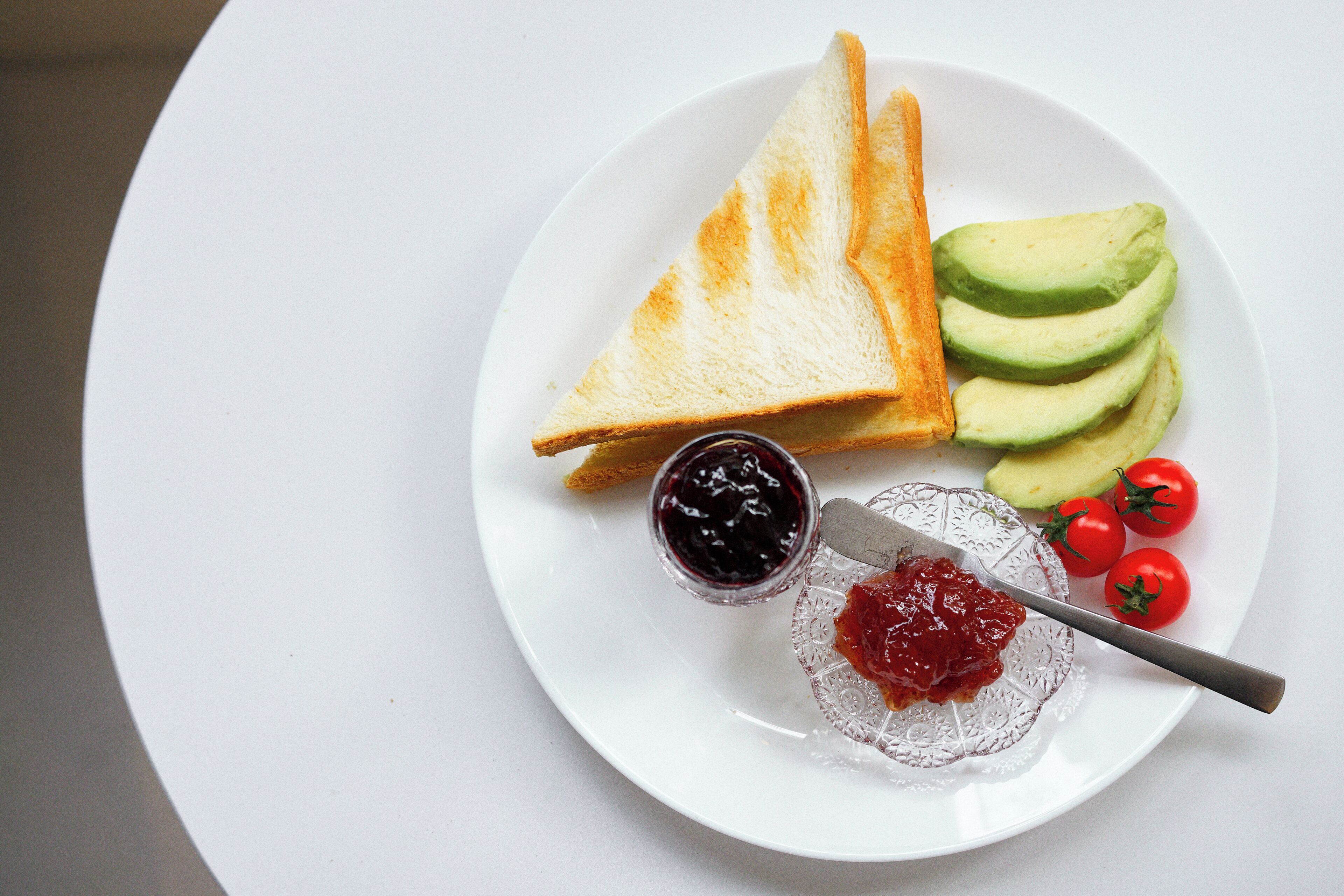 A plate with toast, avocado slices, cherry tomatoes, and jam.