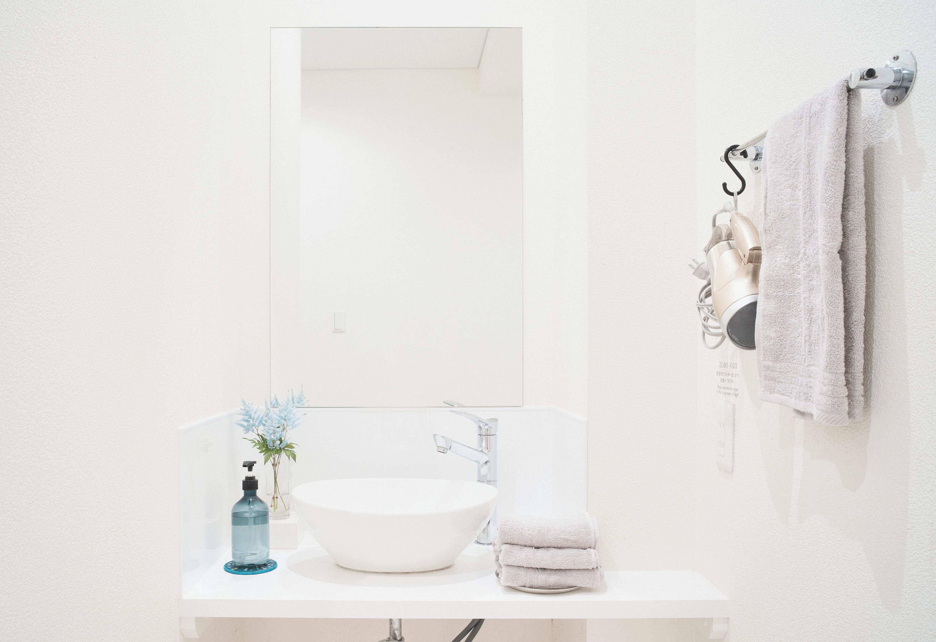 Ein Badezimmer mit weißem Waschbecken, einem Spiegel, einem Handtuchhalter mit Handtüchern und einer Wasserflasche.