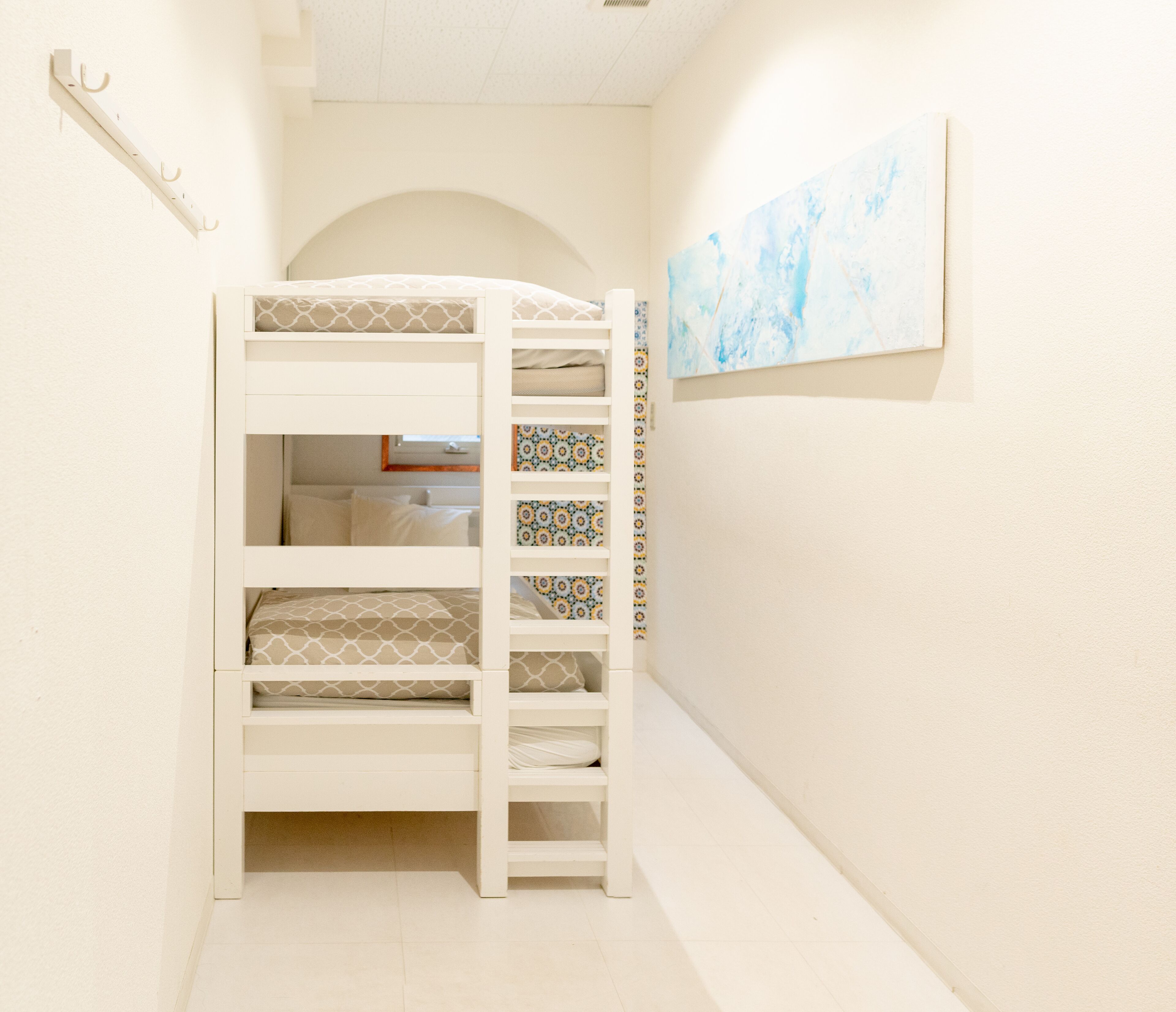 A bunk bed with patterned bedding, a small window, and a blue abstract painting on the wall.