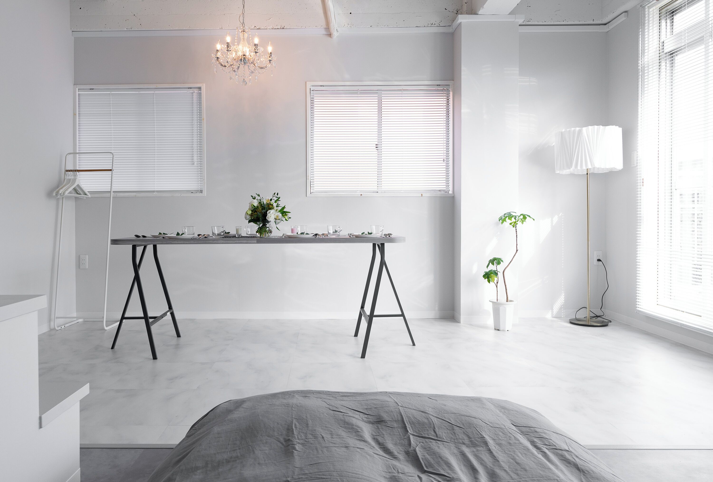 A minimalist room with a bed, a table with a vase of flowers, and a floor lamp.