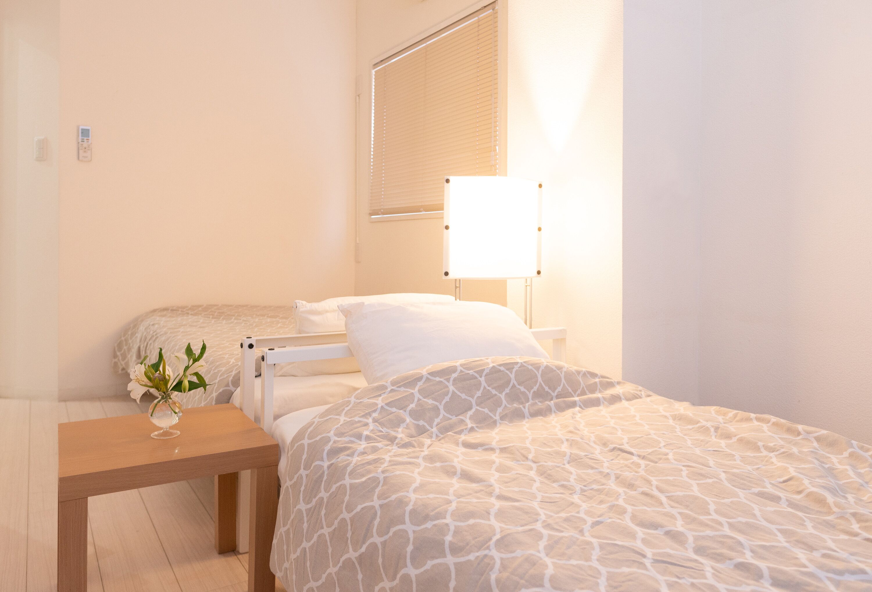 A bedroom with a bed, bedside table, lamp, and a window with blinds.