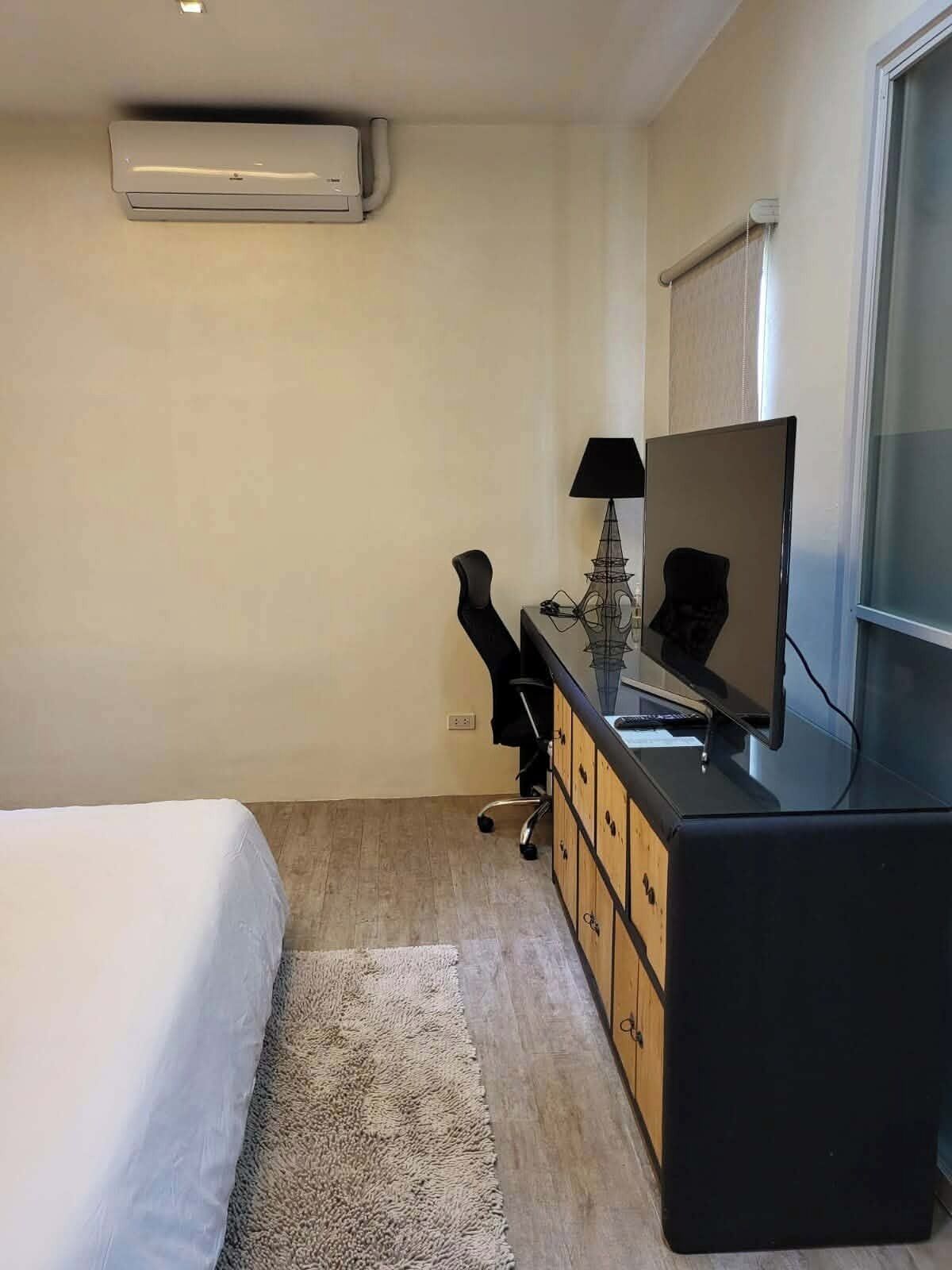 Ein Hotelzimmer mit einem Bett, einem Schreibtisch mit Computer, einer Lampe und einem Fernseher.