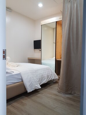 A bedroom with a bed, a nightstand, a TV, and a wooden door.