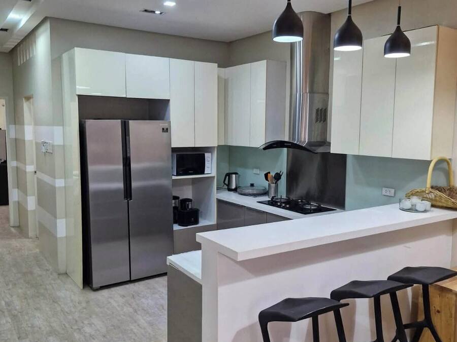A modern kitchen with white cabinets, a stainless steel refrigerator, a central island with bar stools, and pendant lighting.