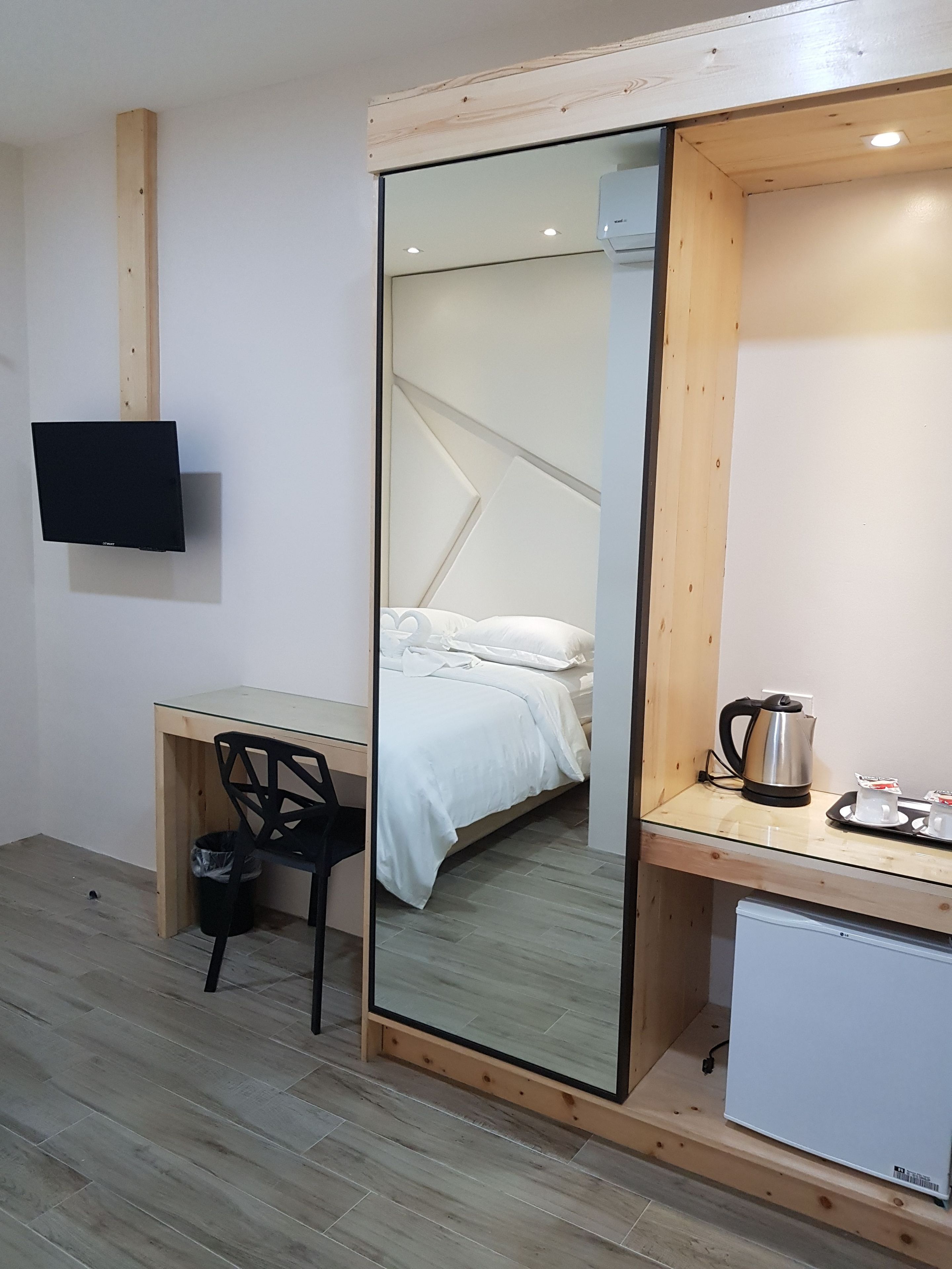 Una habitación de hotel pequeña con cama, escritorio, silla, televisor y kitchenette.