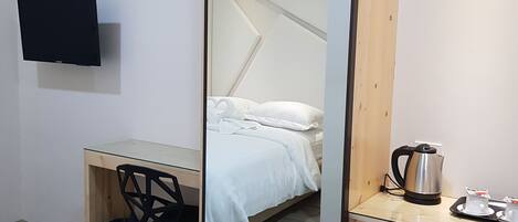 Una habitación de hotel pequeña con cama, escritorio, silla, televisor y kitchenette.