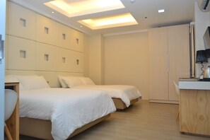 A modern hotel room with two beds, a wooden desk, and a wardrobe.
