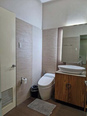 A modern bathroom with a wooden vanity, a white sink, and a toilet.