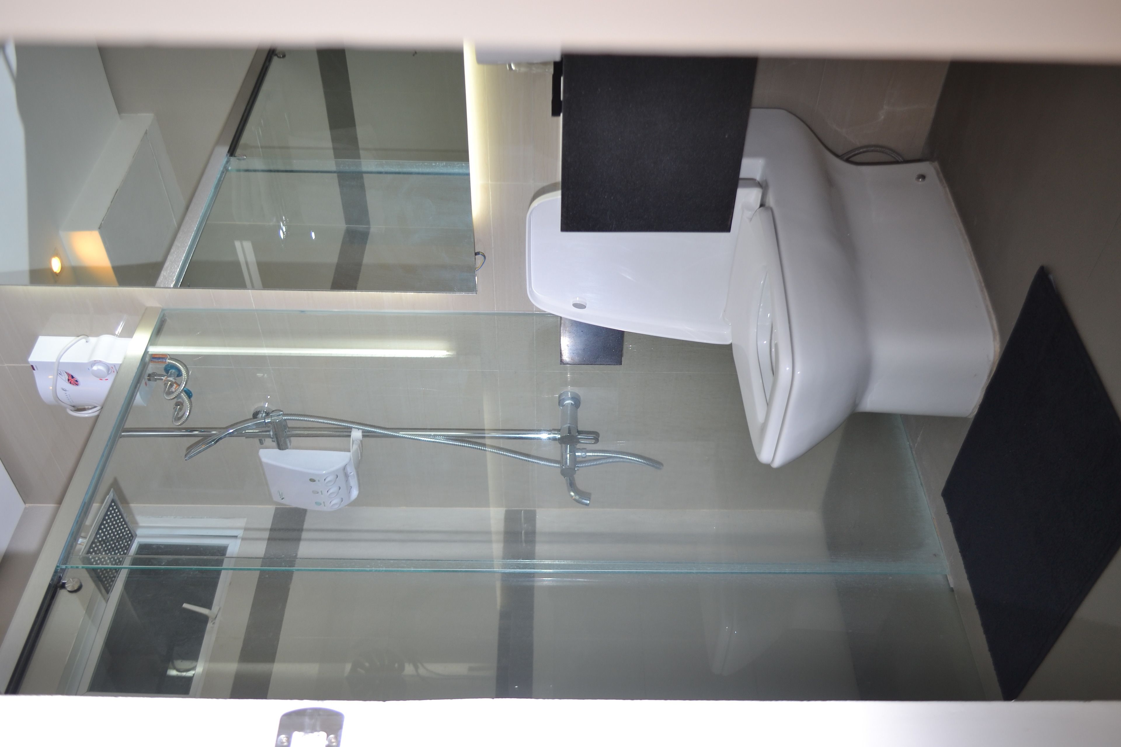 Un baño moderno con cabina de ducha de vidrio, inodoro blanco y un lavamanos pequeño con grifo.