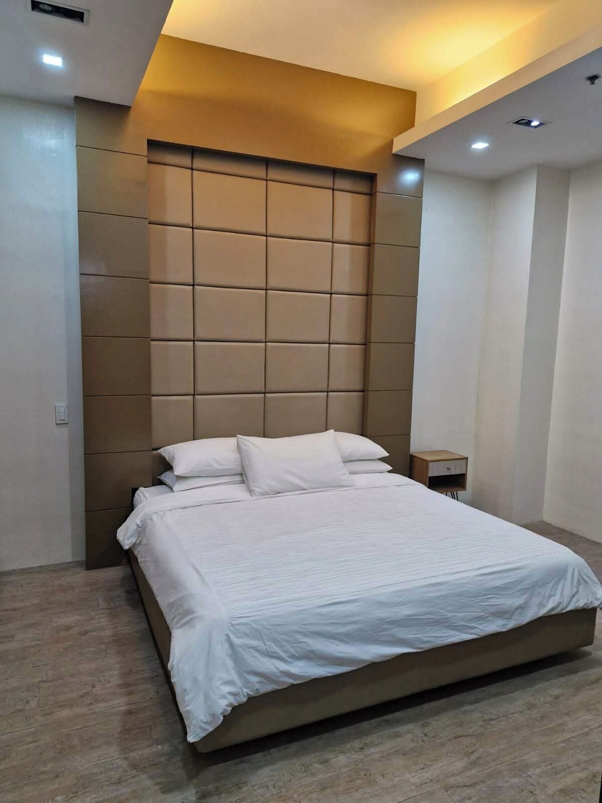 Une chambre à coucher moderne avec un grand lit, une tête de lit au motif géométrique et une petite table de chevet.