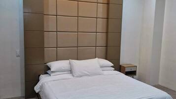 Un dormitorio moderno con una cama grande, cabecera con diseño geométrico y una mesita de noche pequeña.