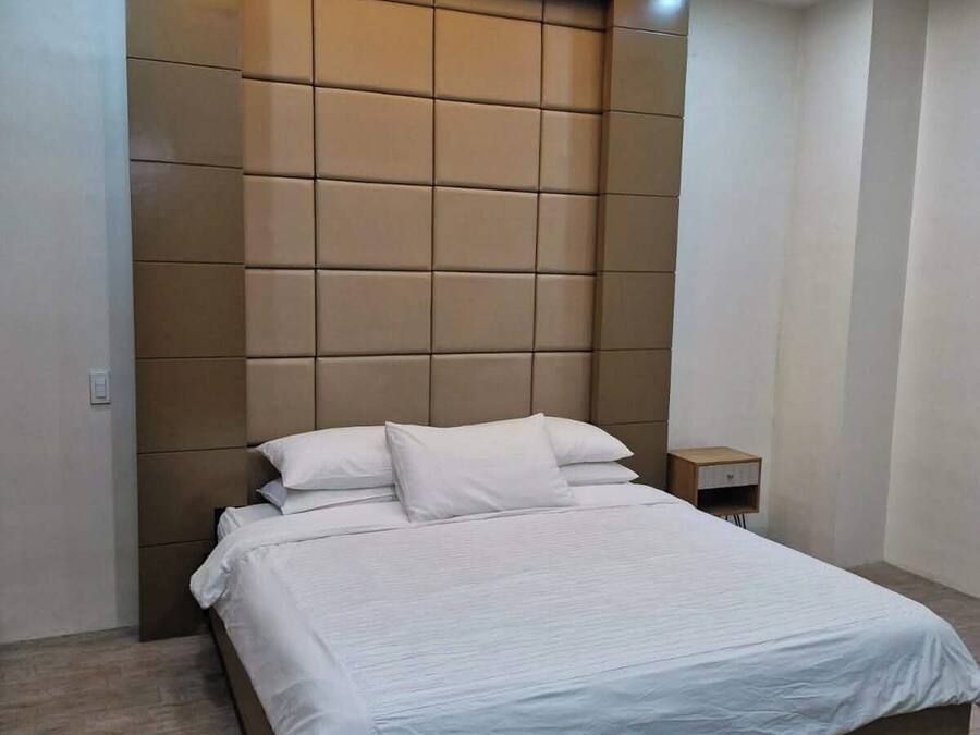 Un dormitorio moderno con una cama grande, cabecera con diseño geométrico y una mesita de noche pequeña.