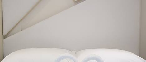 Un lit bien fait, avec du linge de lit blanc et des oreillers, une décoration en forme de cœur réalisée avec des serviettes et un motif géométrique sur le mur.