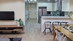 A modern kitchen with a central island, a dining area with a table and chairs, and a TV mounted on the wall. - F2M Tower (Legazpi)