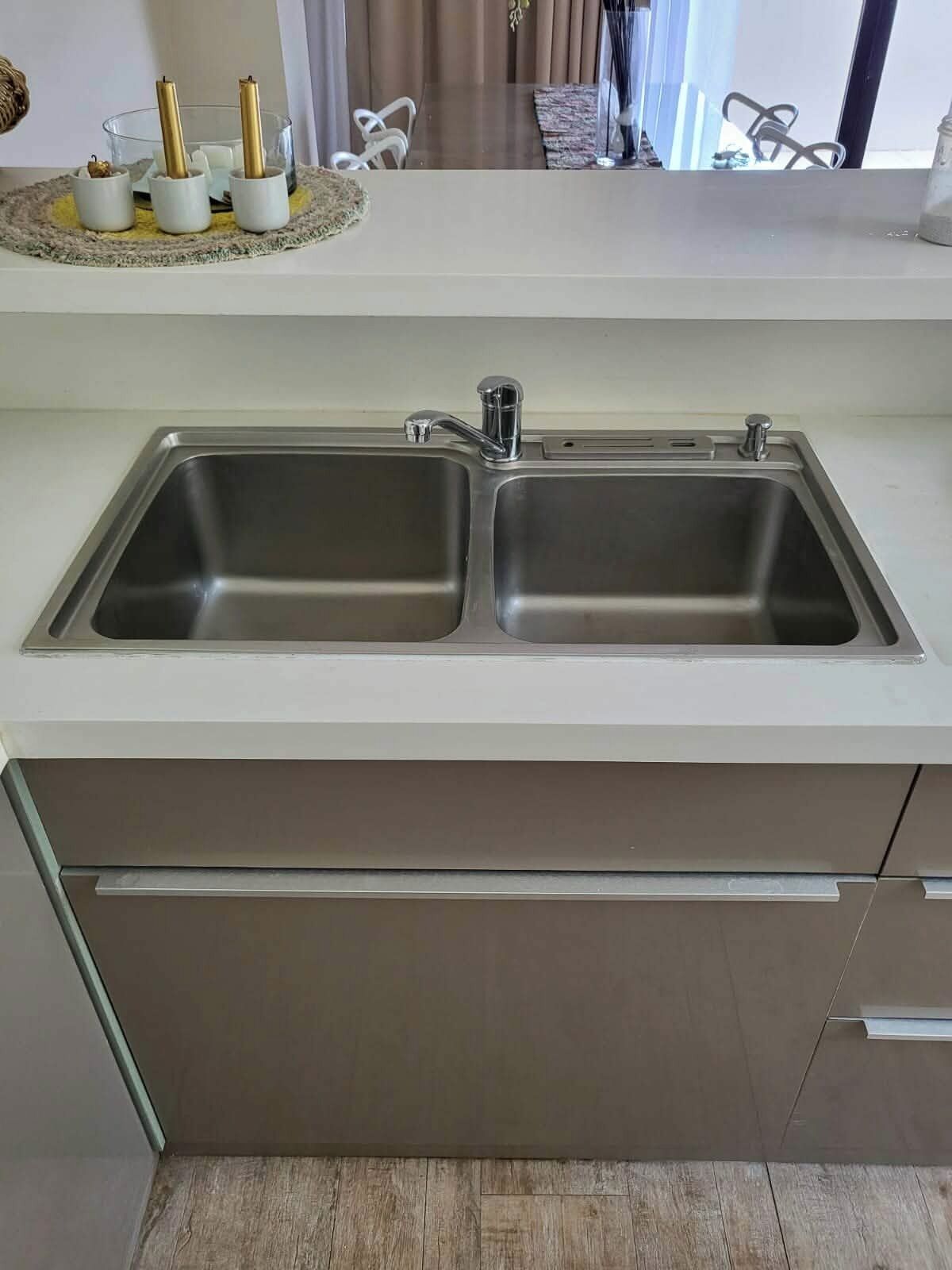 A kitchen with a double stainless steel sink, a white countertop, and a wooden floor.