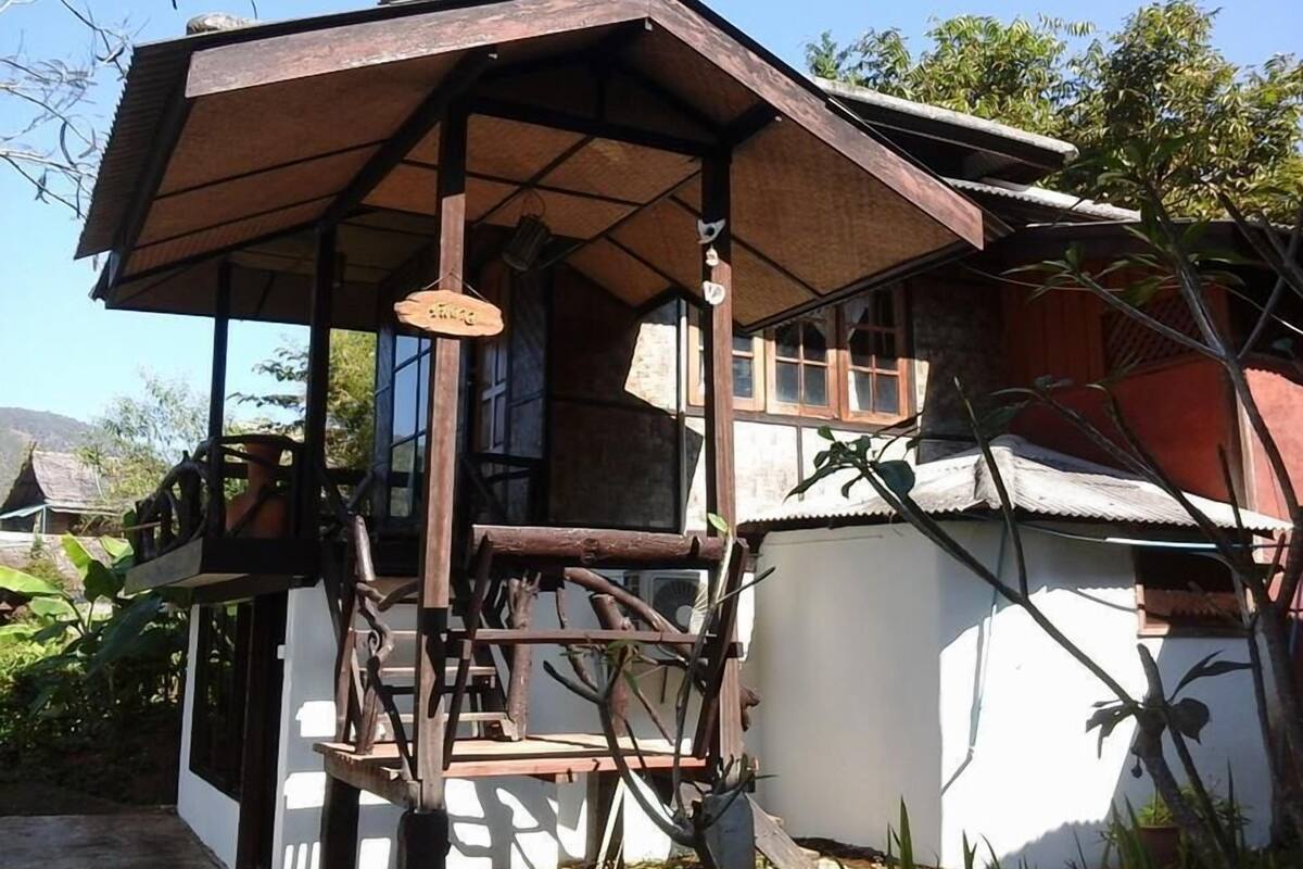 A traditional wooden house with a porch, a sign hanging from the porch, and a window.
