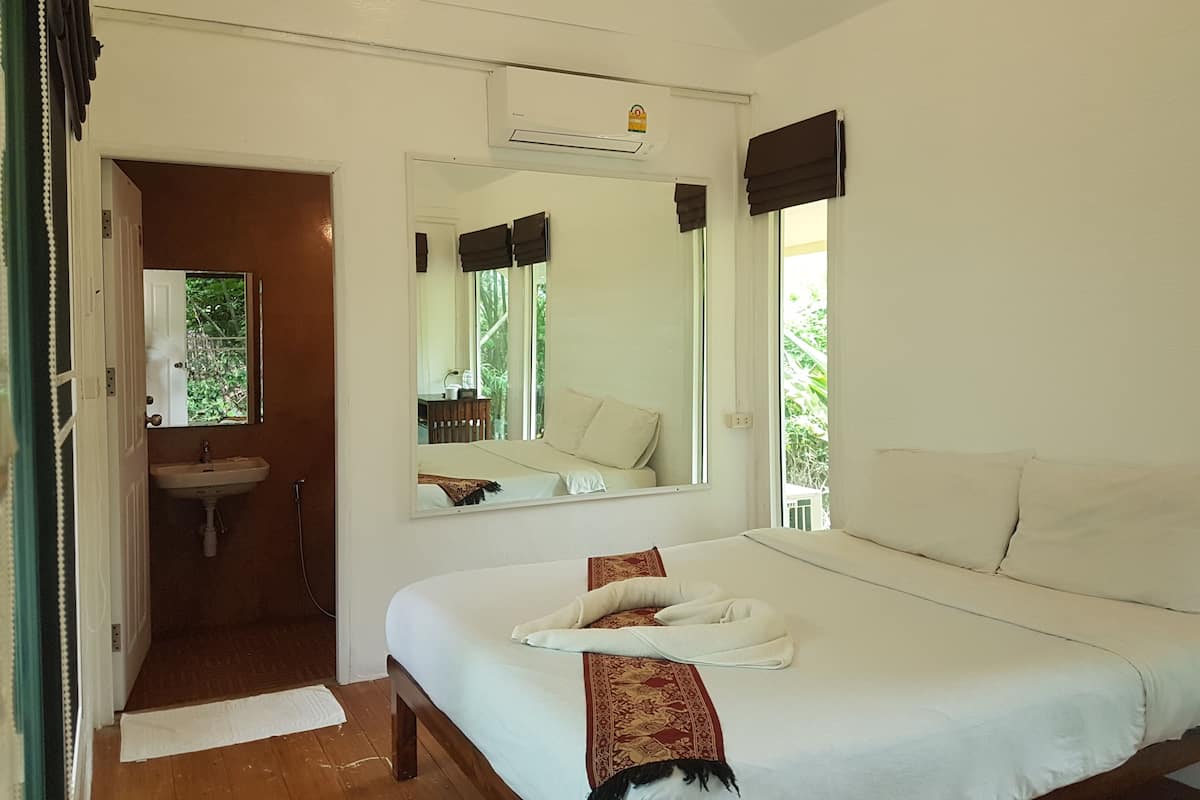A bedroom with a bed, a mirror, a window, and a bathroom visible through an open door.
