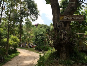 Schild für das Chang Pai Resort, umgeben von üppigem Grün und einem unbefestigten Weg.