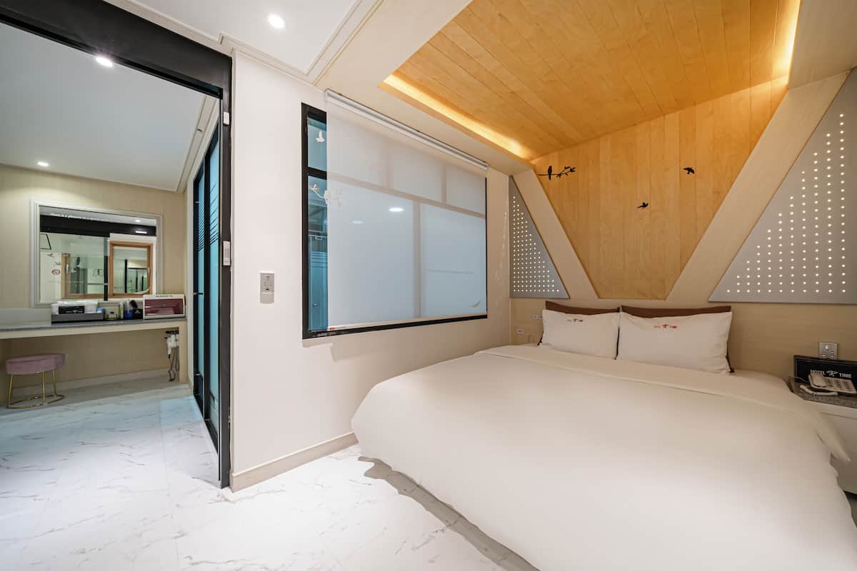 A modern hotel room with a large bed, a wooden ceiling, and a large window.