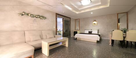 A modern hotel room with a sofa, a bed, a dining table, and a small TV.