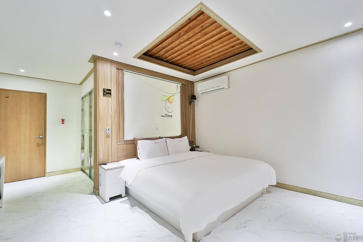 A modern bedroom with a wooden ceiling, a bed with white bedding, a bedside table, and a nightstand.