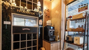 A coffee shop with a counter, a coffee machine, and a display of bread and pastries.