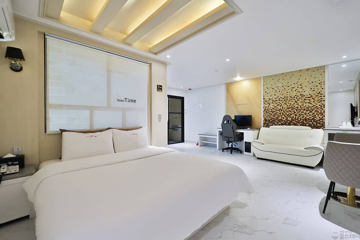 A modern hotel room with a large bed, a desk, a sofa, and a mirror.