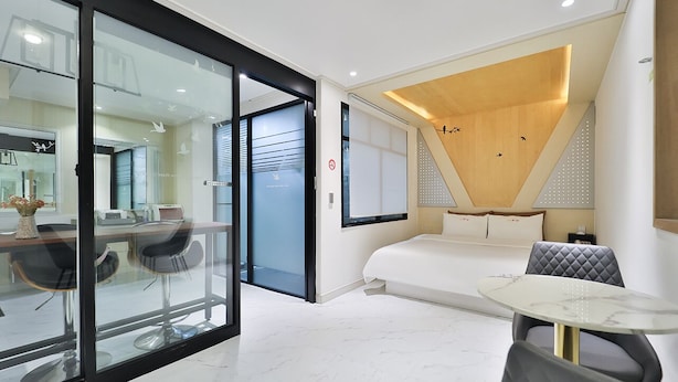 A modern hotel room with a glass partition, a bed, a small table, and a seating area.