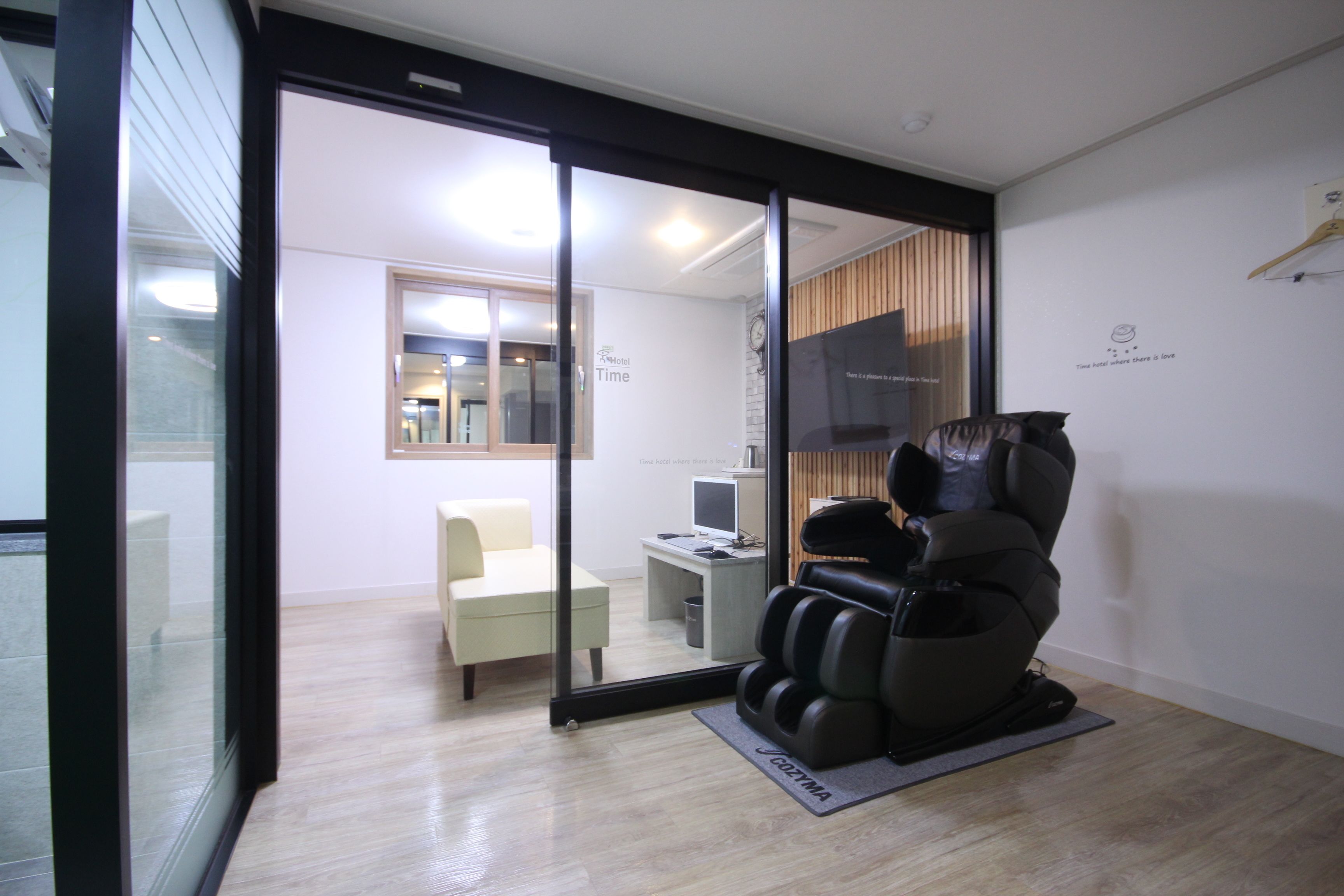 A massage chair in a room with a glass door leading to a seating area and a desk with a computer.