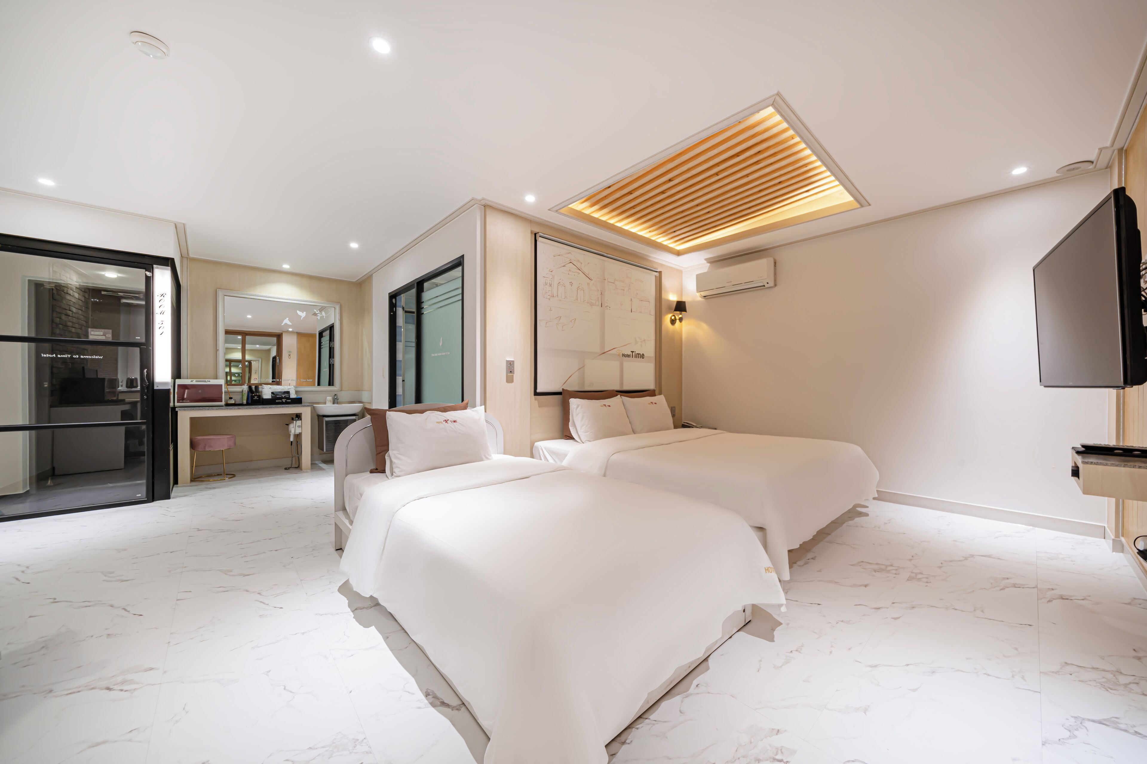 A hotel room with two beds, a kitchenette, a bathroom, and a TV.