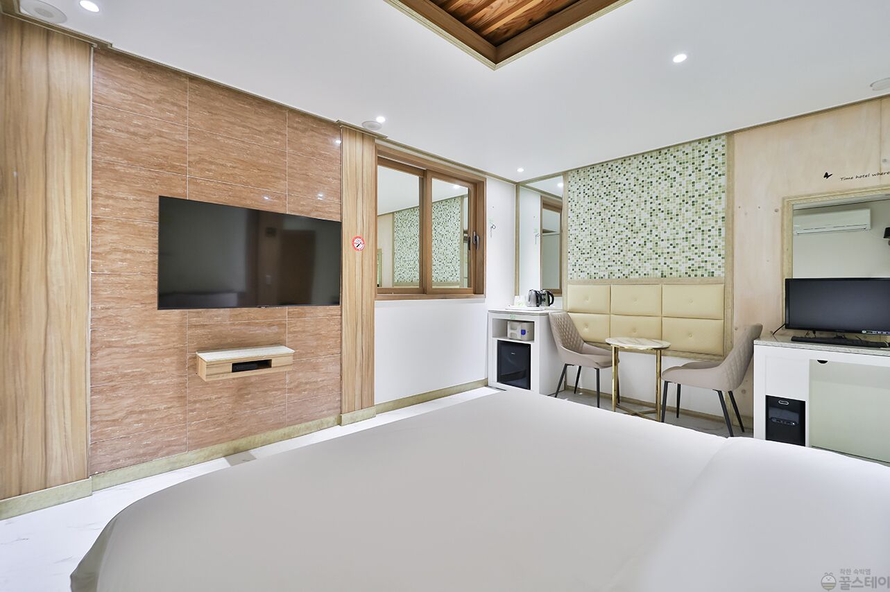 Une chambre d’hôtel moderne dotée d’un grand lit, d’un téléviseur fixé au mur, d’un petit coin salon avec un canapé et des fauteuils, et d’un mini-bar.