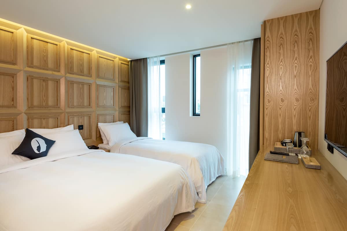 Habitación de hotel con dos camas, cabecero de madera, un ventanal grande y un panel de pared de madera.