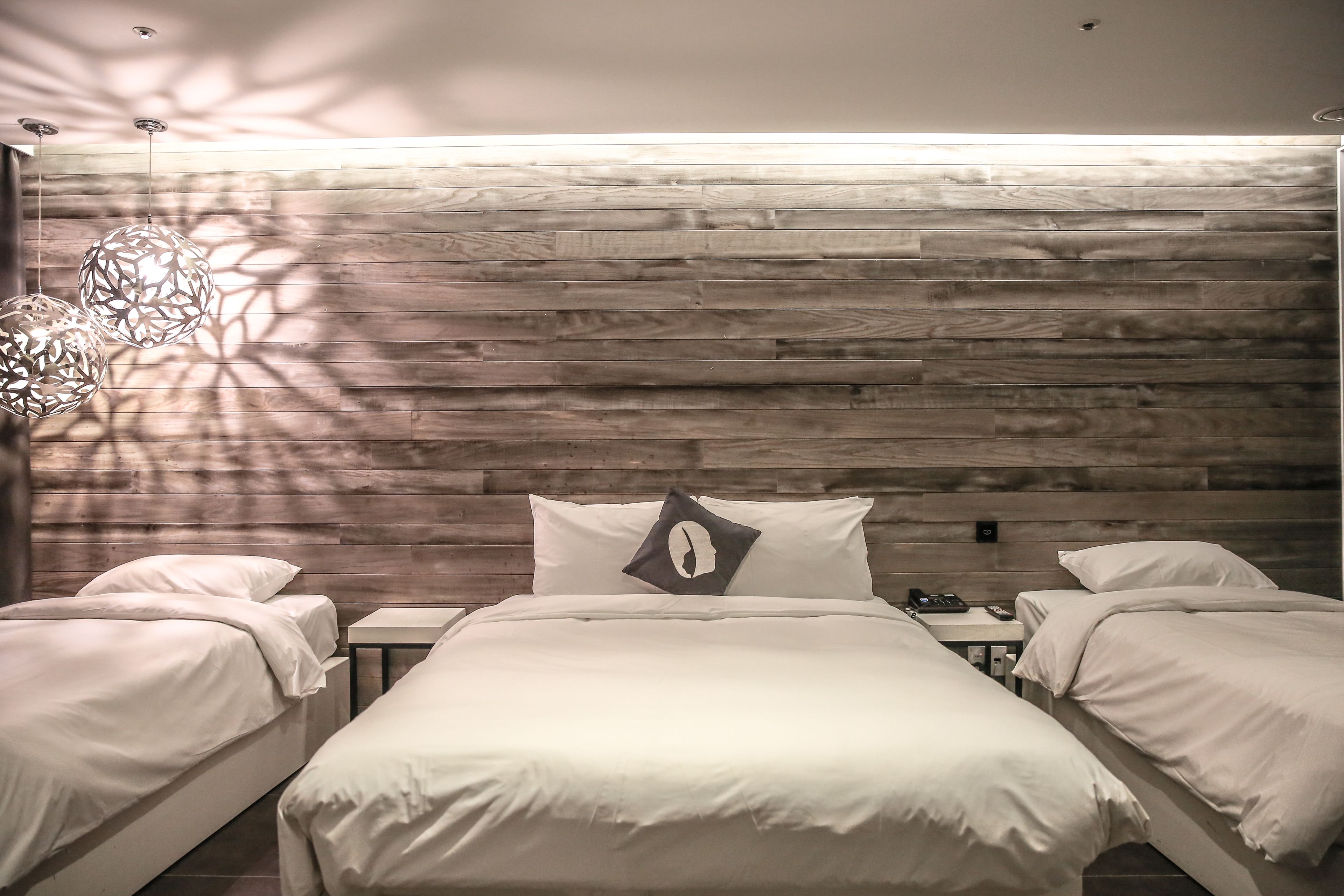 A room with two beds, a wooden wall, and a modern light fixture.