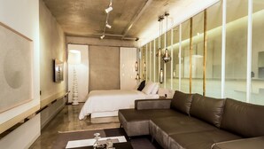 A modern hotel room with a bed, sofa, and a large window.