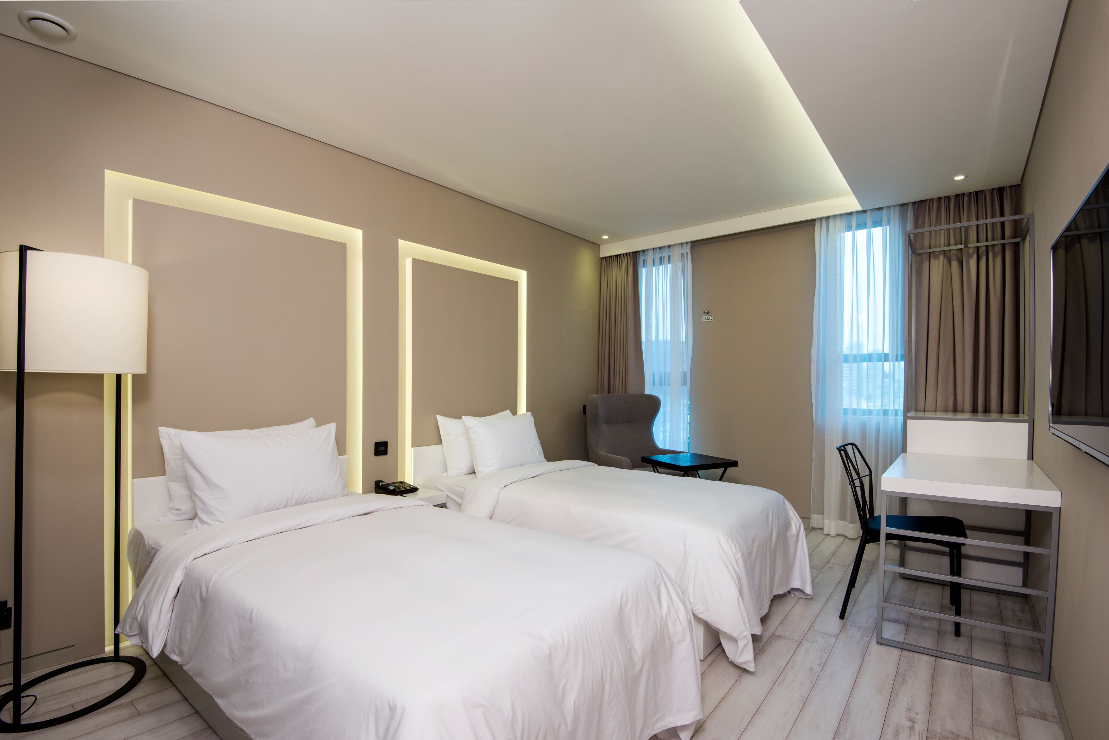 Una habitación de hotel con dos camas, un escritorio, una silla y una lámpara.