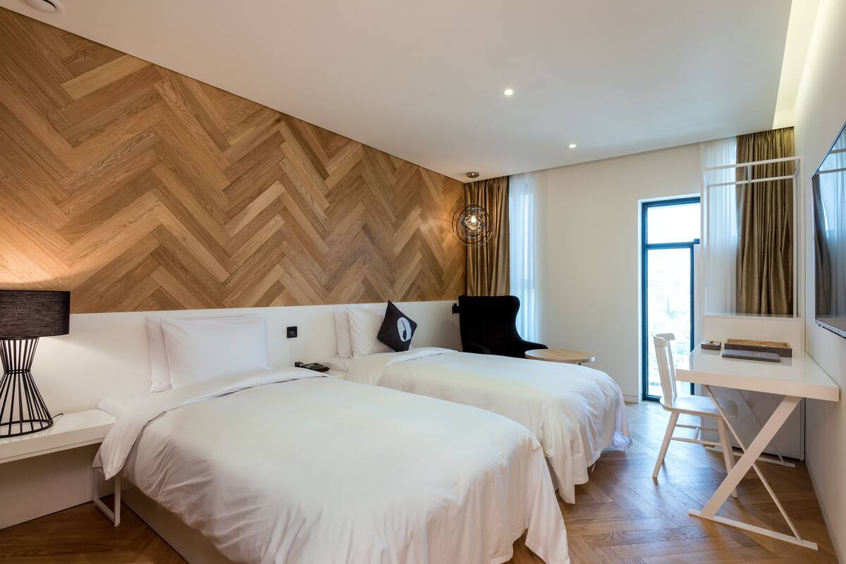 Una habitación de hotel moderna con dos camas, un escritorio y un ventanal amplio.