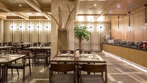 A restaurant with multiple tables and chairs, a central column with a tree, and a kitchen area visible on the right.