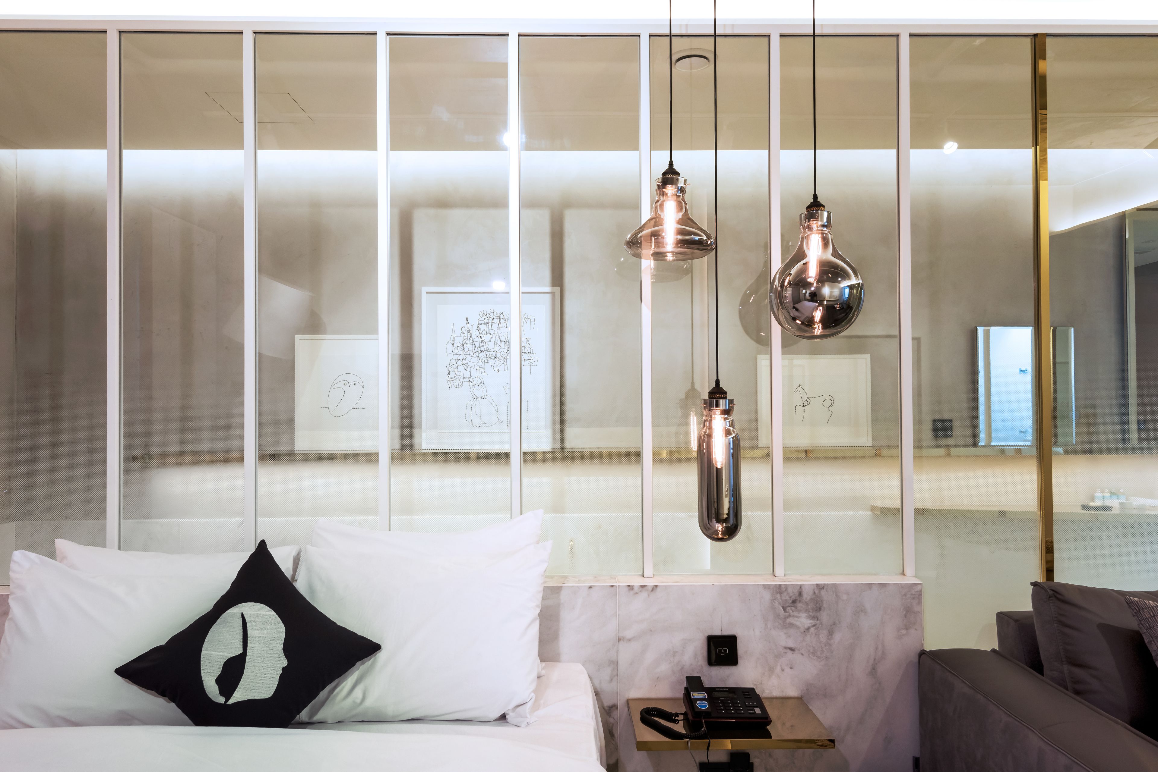 A modern hotel room with a bed, a bedside table with a phone, and a large window with artwork.