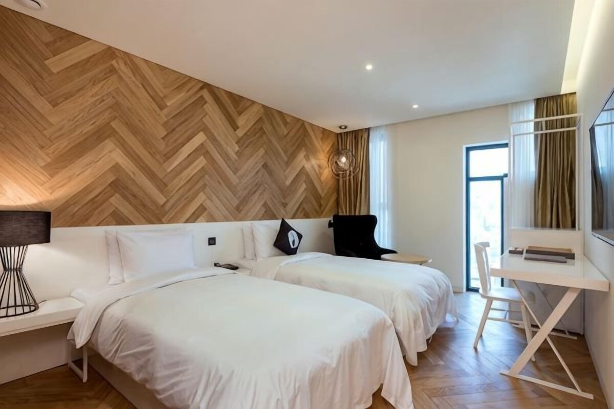 Habitación de hotel con dos camas, un escritorio y un ventanal grande.