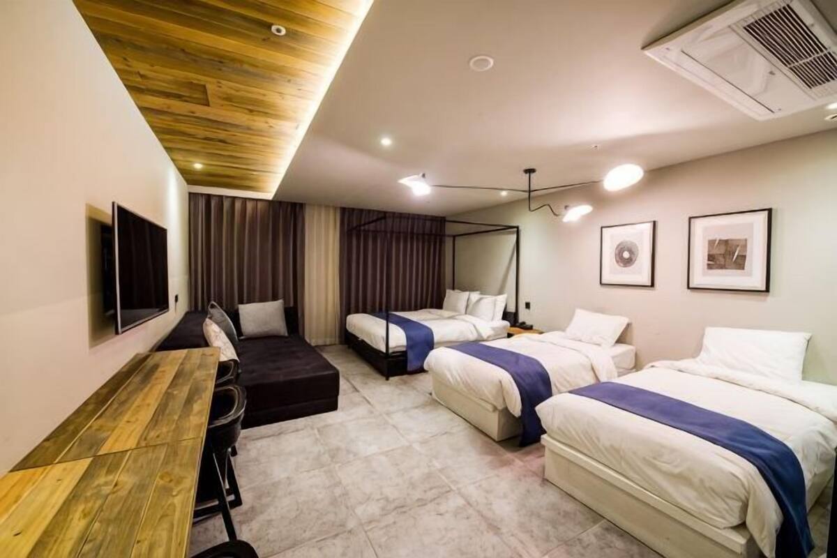 Habitación de hotel con dos camas, un escritorio, un televisor y un ventilador de techo.