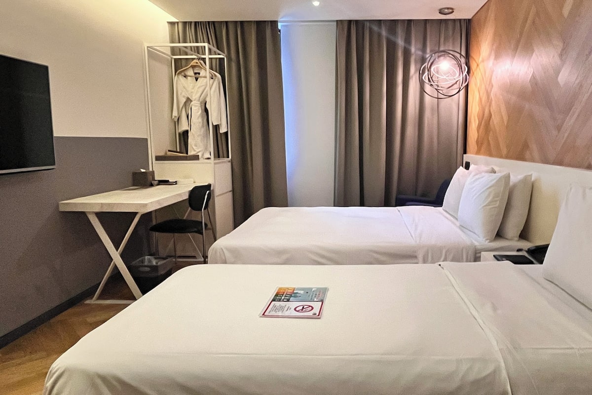 Habitación de hotel con dos camas, un escritorio, una silla y un televisor.