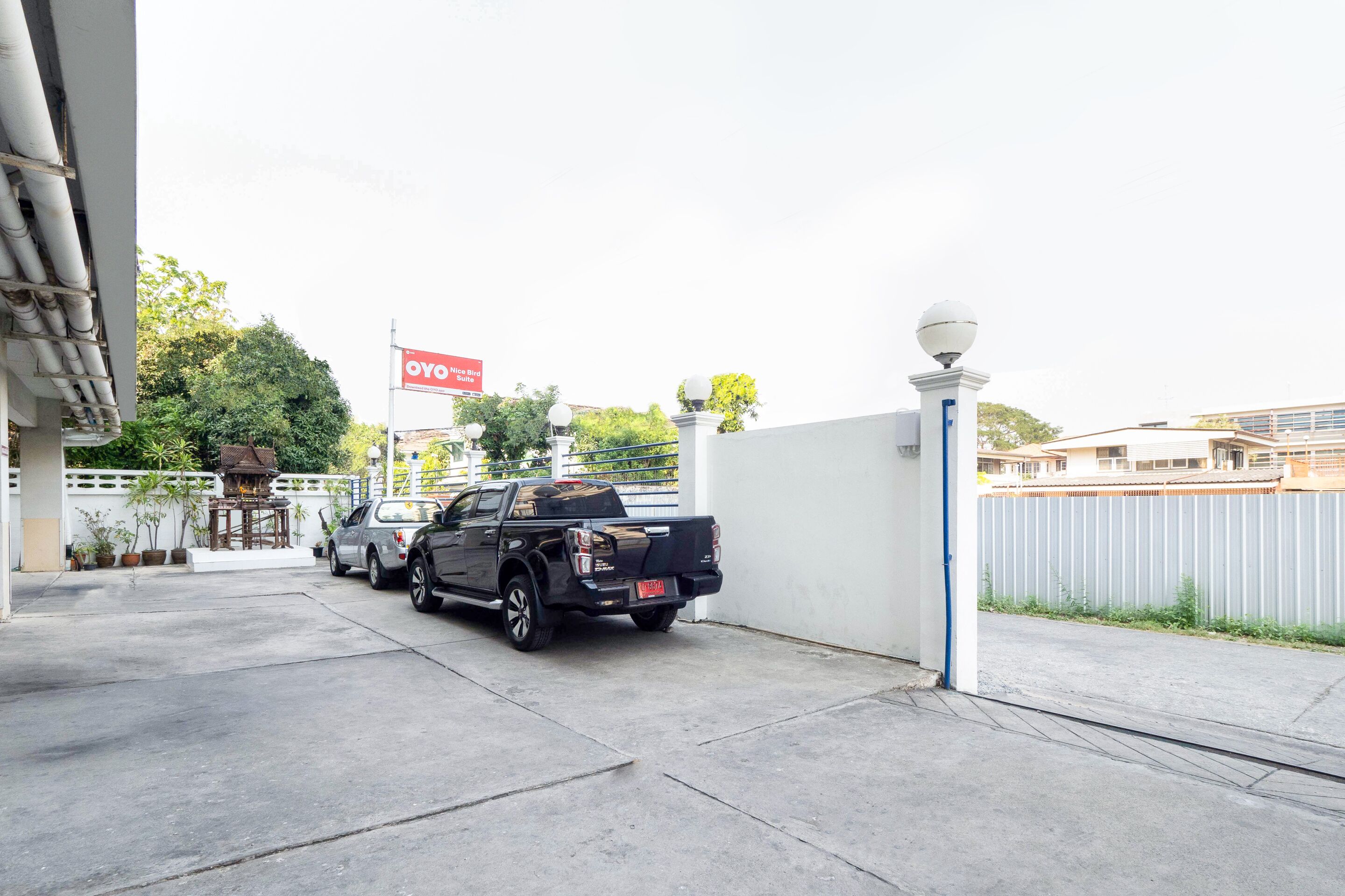A parking area with a black pickup truck and a silver car, a white fence, and a red sign in the background.