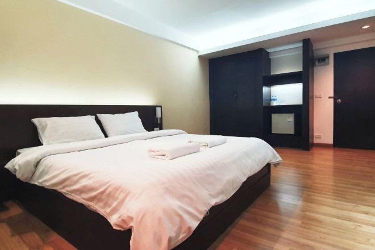 A modern hotel room with a large bed, wooden flooring, and a built-in wardrobe.