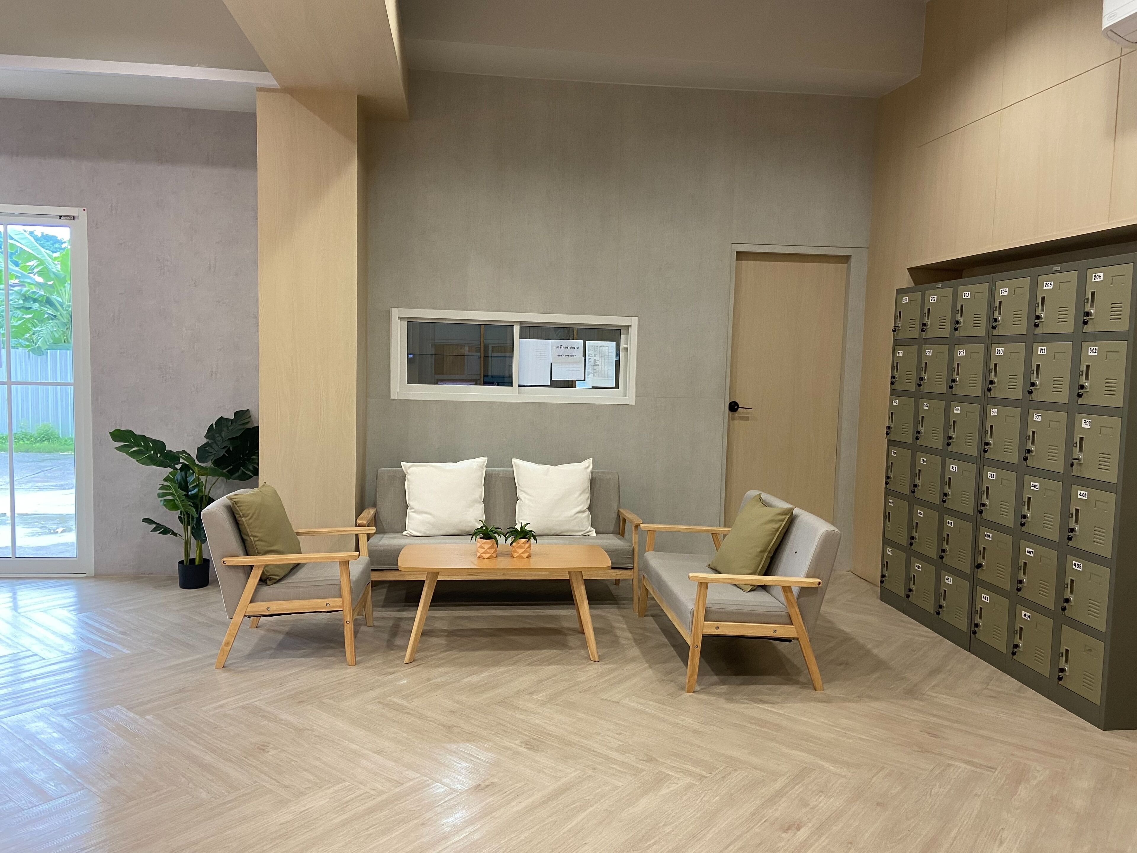 A modern interior with a wooden floor, a sofa set, a small table, a potted plant, and a row of lockers.