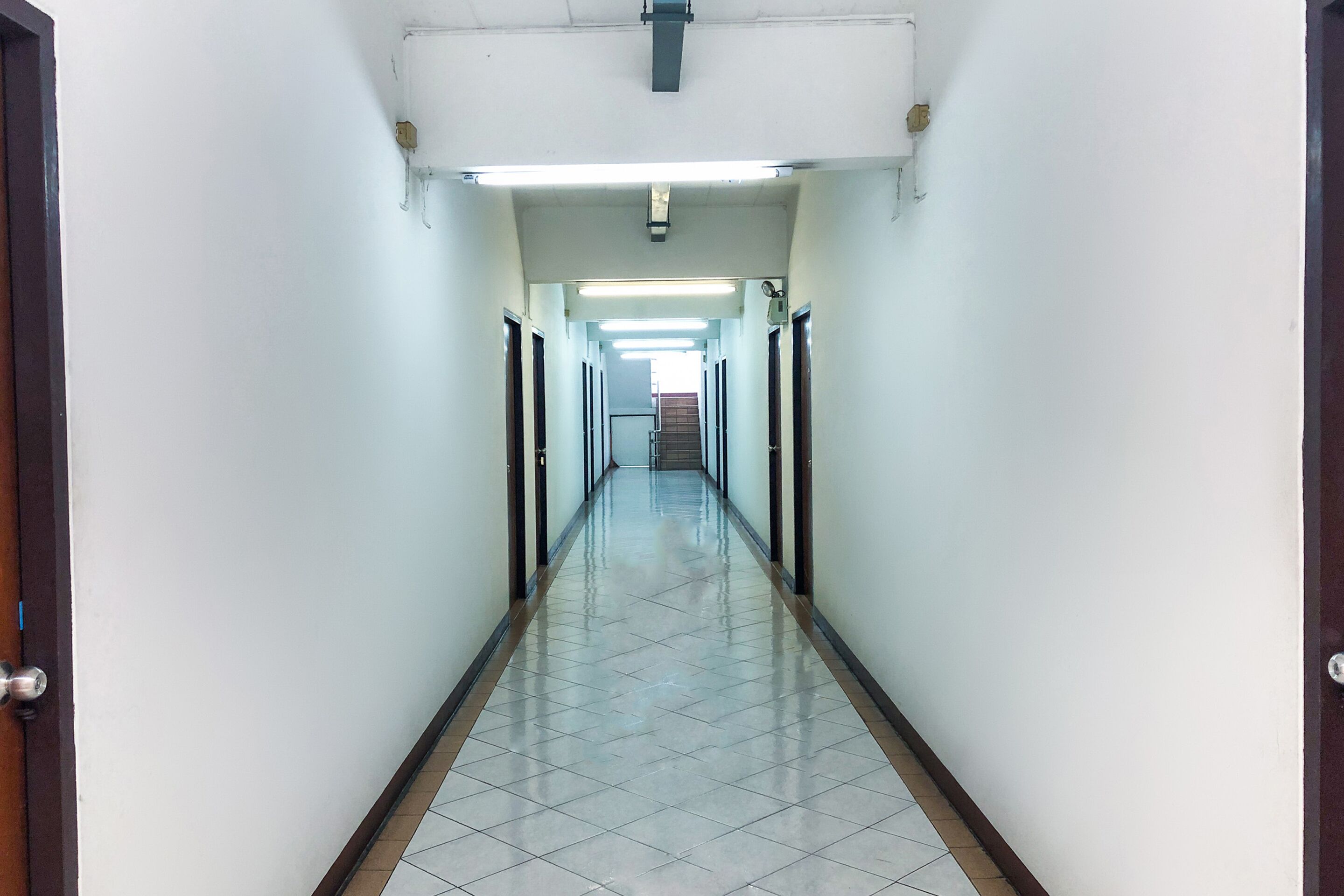 A long, narrow hallway with white walls and a tiled floor, leading to a staircase at the end.