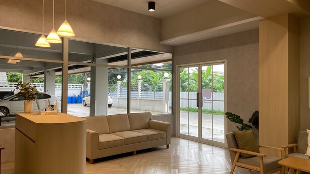 Un área de recepción con sofá, sillas de madera, mostrador de recepción, lámparas colgantes y vistas al estacionamiento.